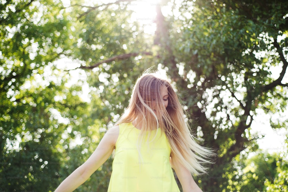 Beautiful young woman with long blowing blonde hair in neon yellow tank top. Sunny summer day.