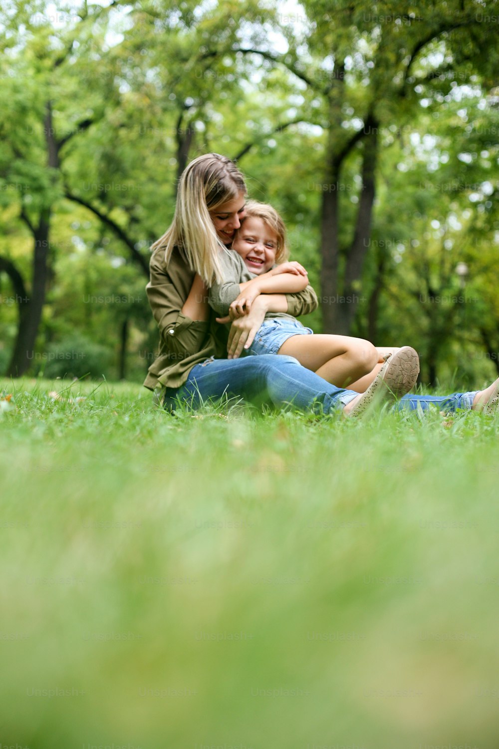 Menina sentada no colo da mãe. Mãe alegre com a filha sentada na grama. Espaço para cópia.