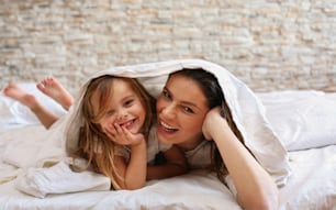 Happy mother and daughter under blanket.Looking at camera.