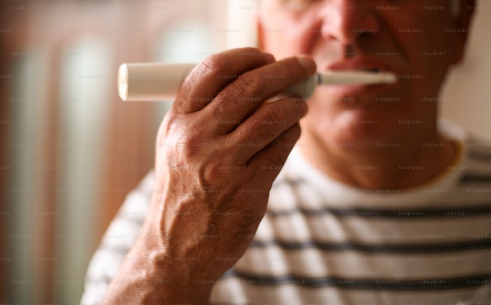 Body part of senior man brushing teeth. Focus is on hand.