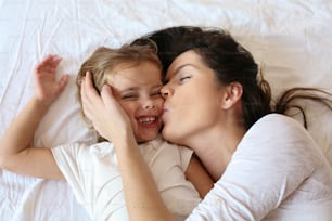 Mother and daughter enjoy in bed at home.