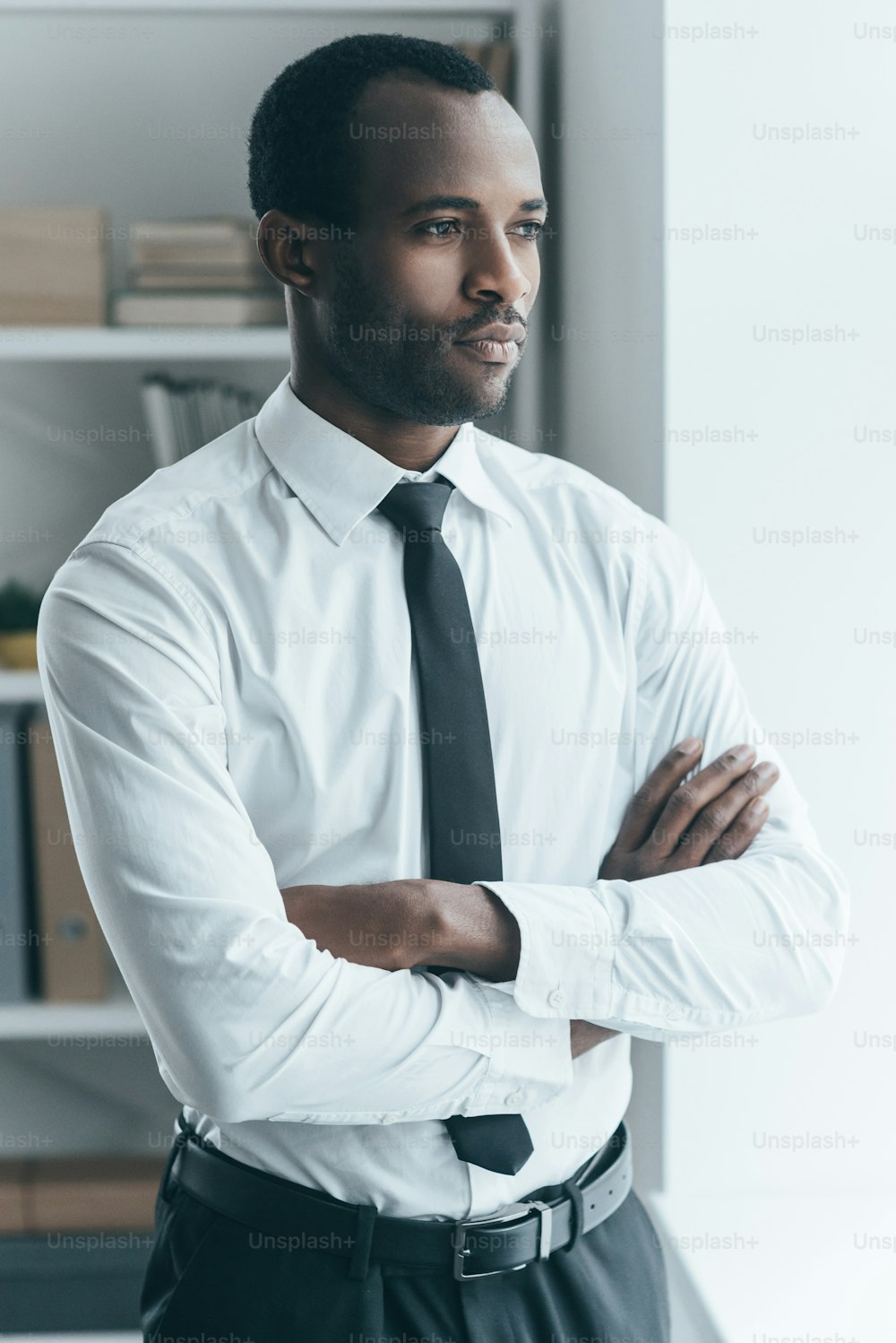 Handsome young African man keeping arms crossed and looking somewhere while standing in creative office