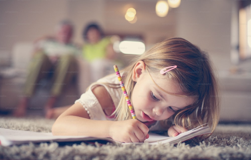 Cute little girl laying on floor and writing.