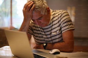 Senior Mann ist enttäuscht, benutzt Laptop zu Hause.