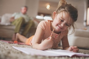 Cute little girl laying on floor and writing.