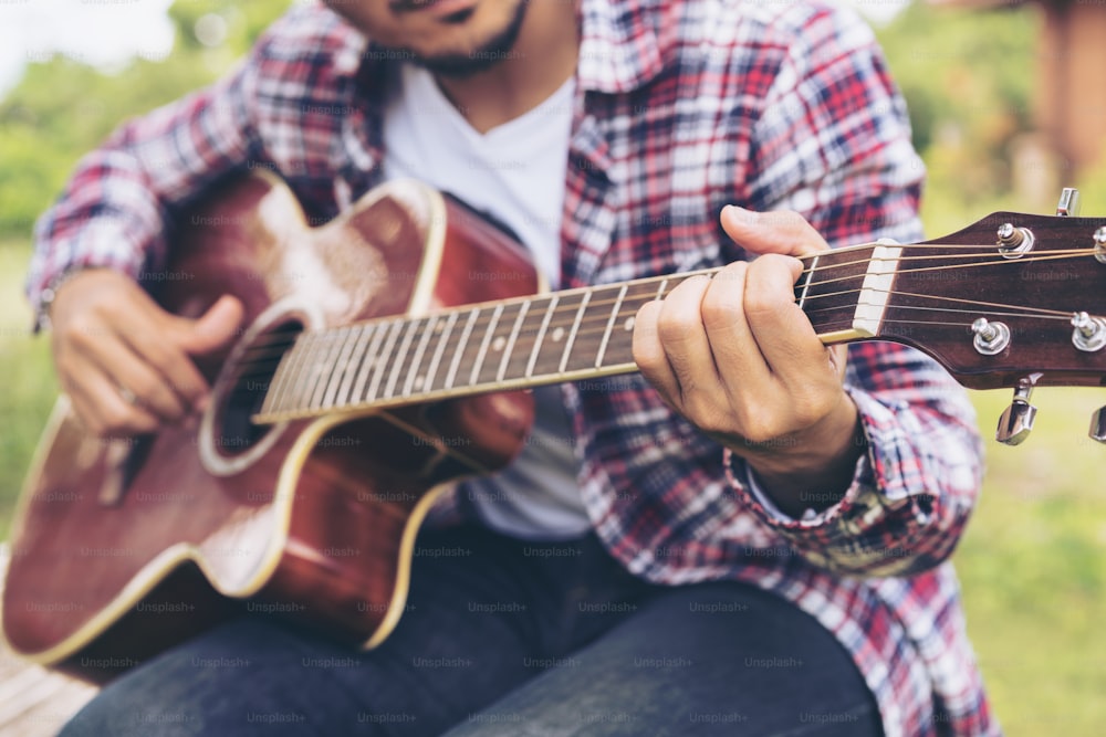 Man 's hand playing guitar, sitting on green grass. Nature background. Music, guitar and nature. Country folk song from acoustic guitar. Man holding his guitar.