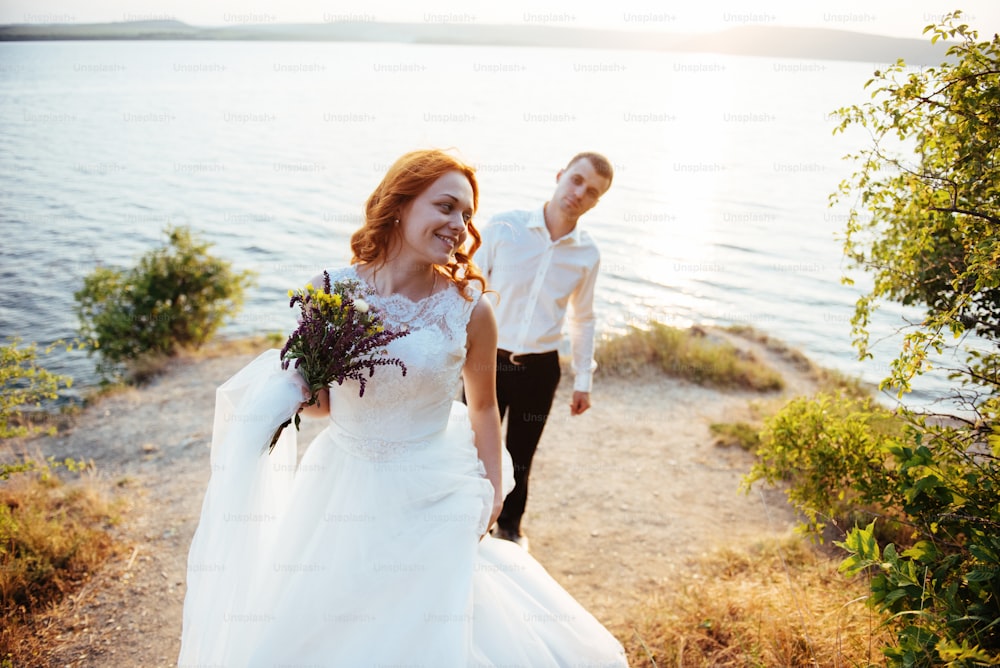 beautiful lovely blonde bride and groom classy on the rocks, amid the sea at sunset.