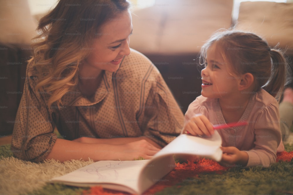 Beautiful blonde Caucasian girl lying on the floor with her mother and drawing.