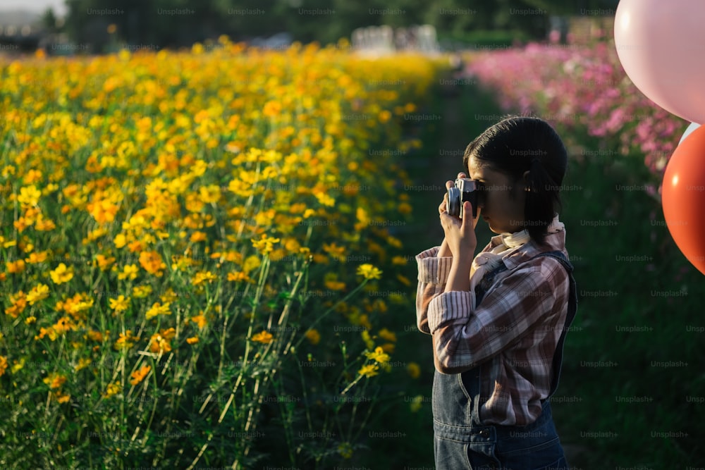 Chica asiática tomar una foto con una cámara vintage sobre el campo del cosmos.