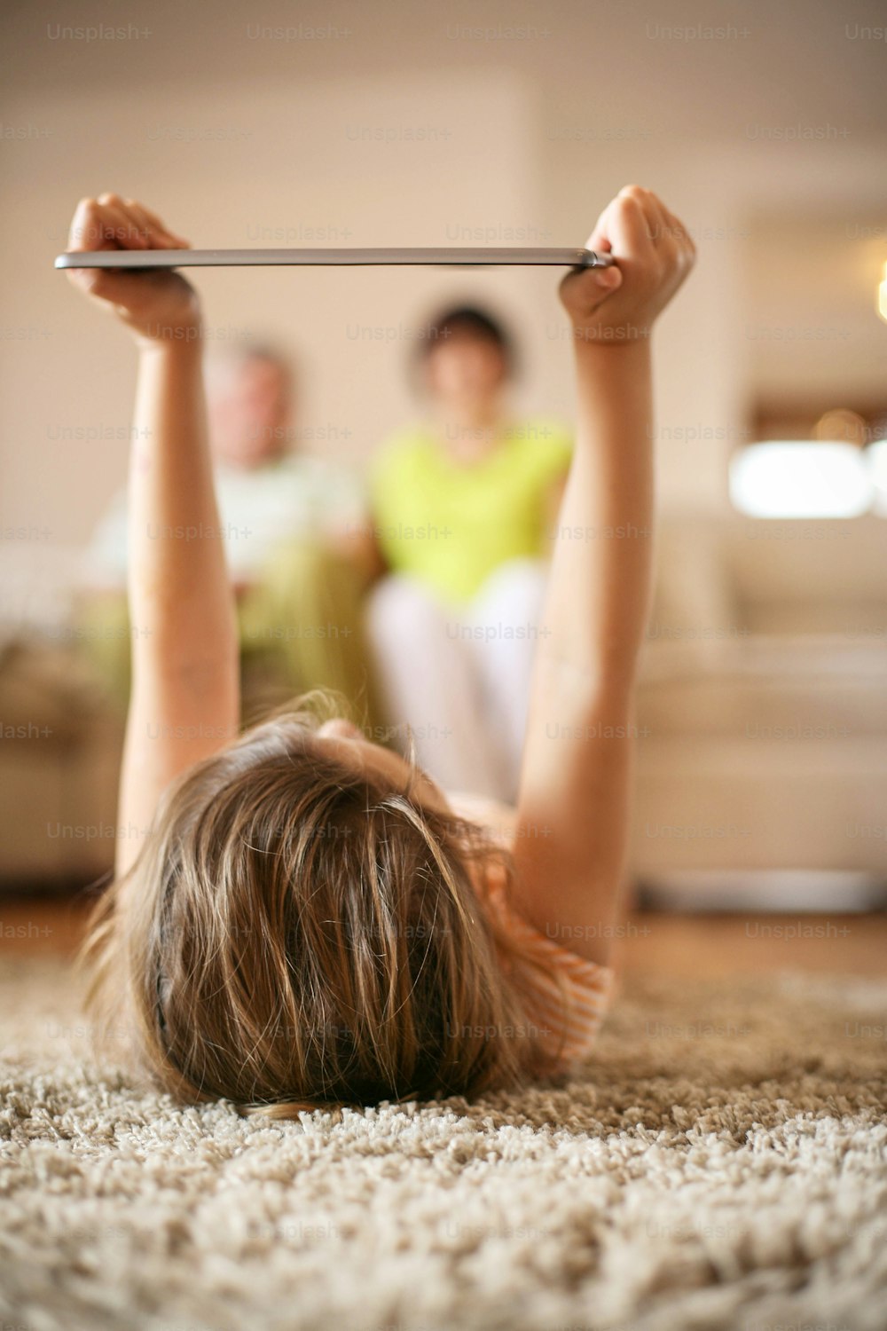 Granddaughter using tablet in living room while grandparents in background