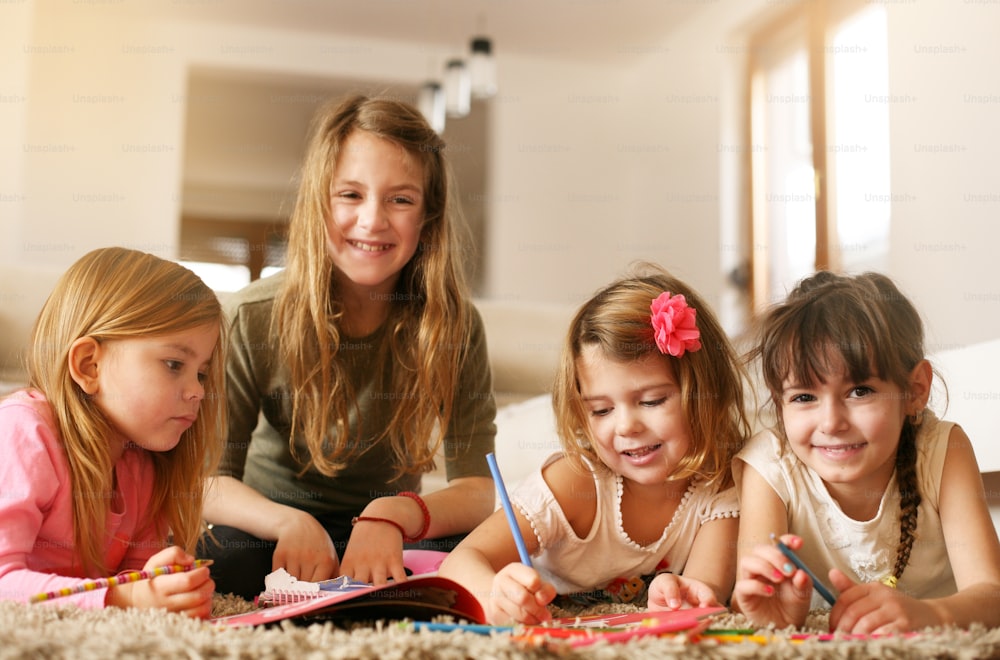 Four girls lying on the floor and write their homework. Looking at camera. Looking at camera.