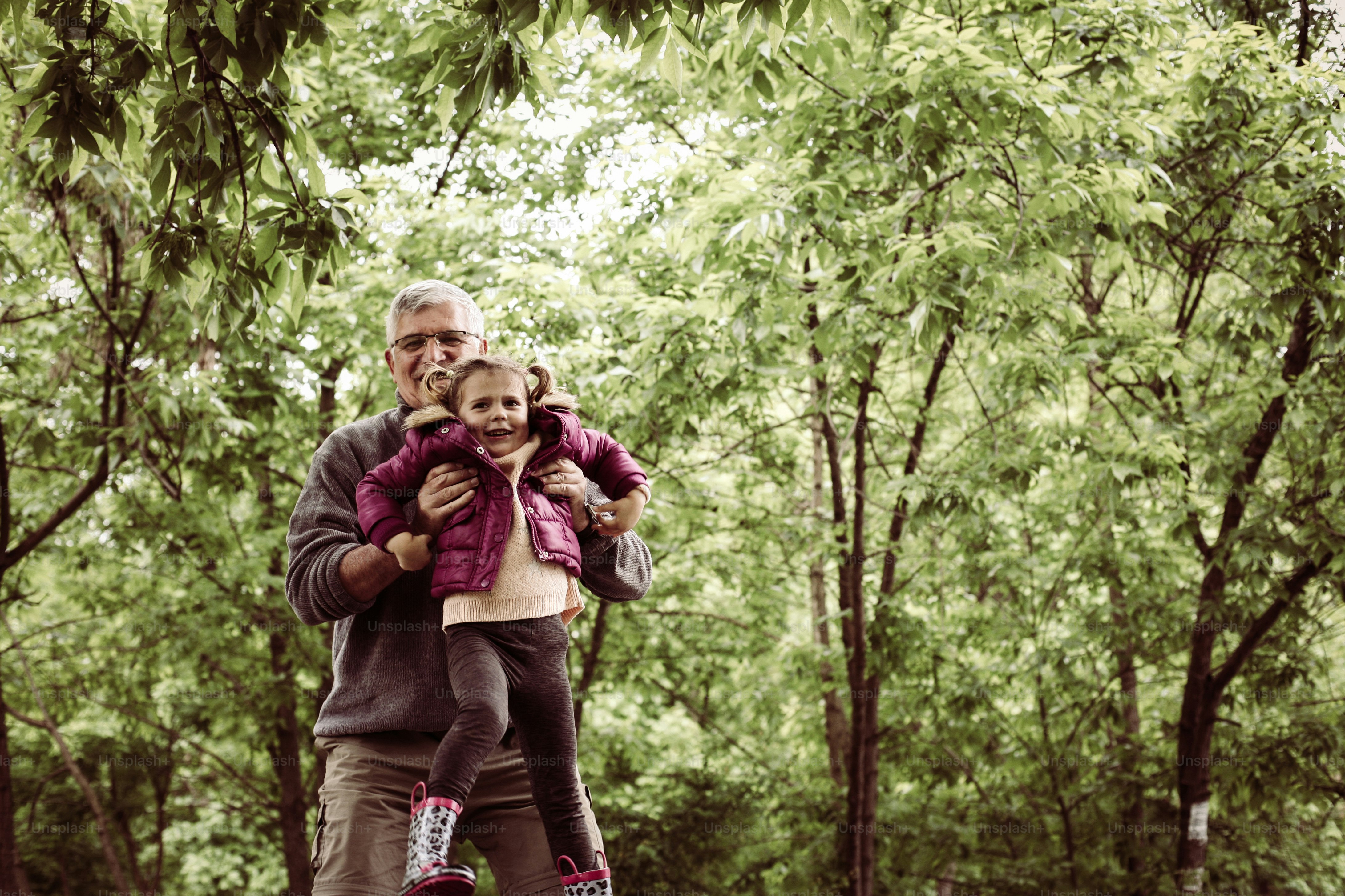 Happy kid playing with grandfather in the park.