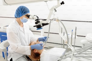 Female dentist looking at dental equipment and drilling in mouth of woman. Patient lying on chair and looking up