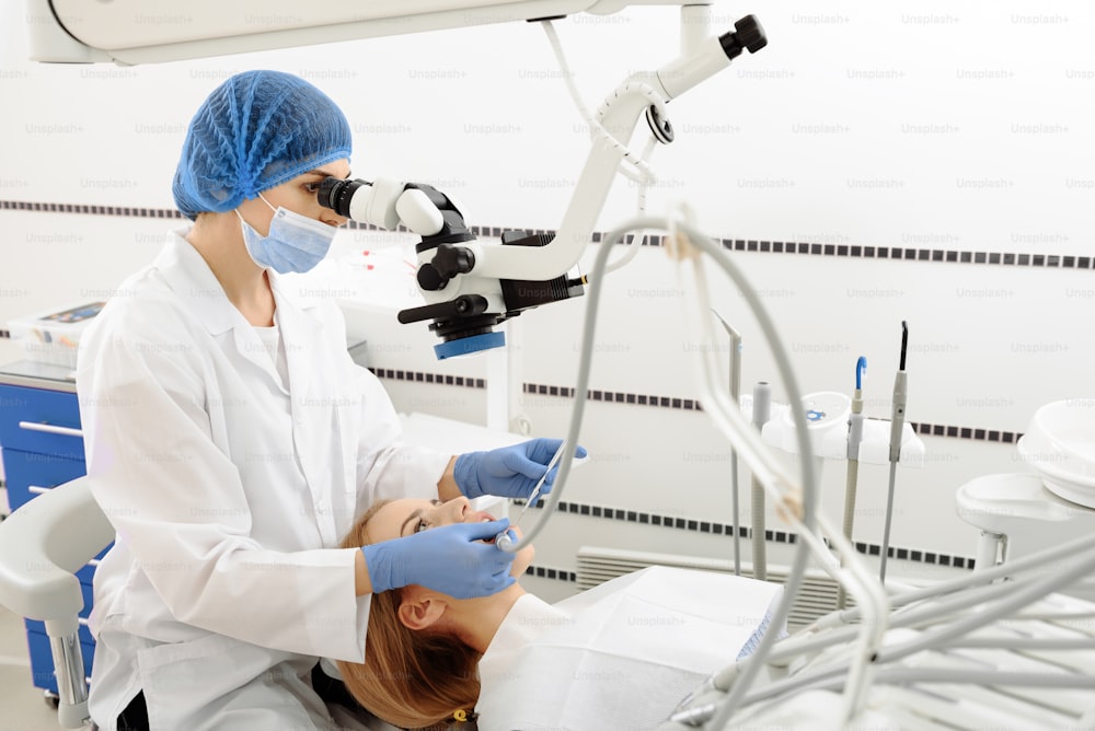 Una dentista mirando equipos dentales y perforando en la boca de una mujer. Paciente acostado en una silla y mirando hacia arriba