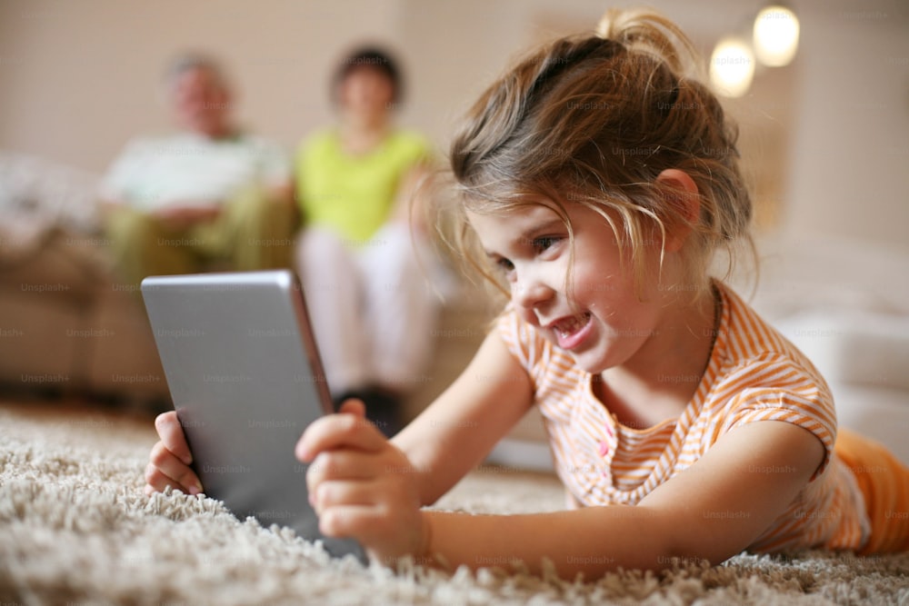 Granddaughter using tablet in living room while grandparents in background