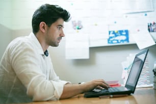 Joven diseñador trabajando en una computadora portátil en la oficina de su casa.