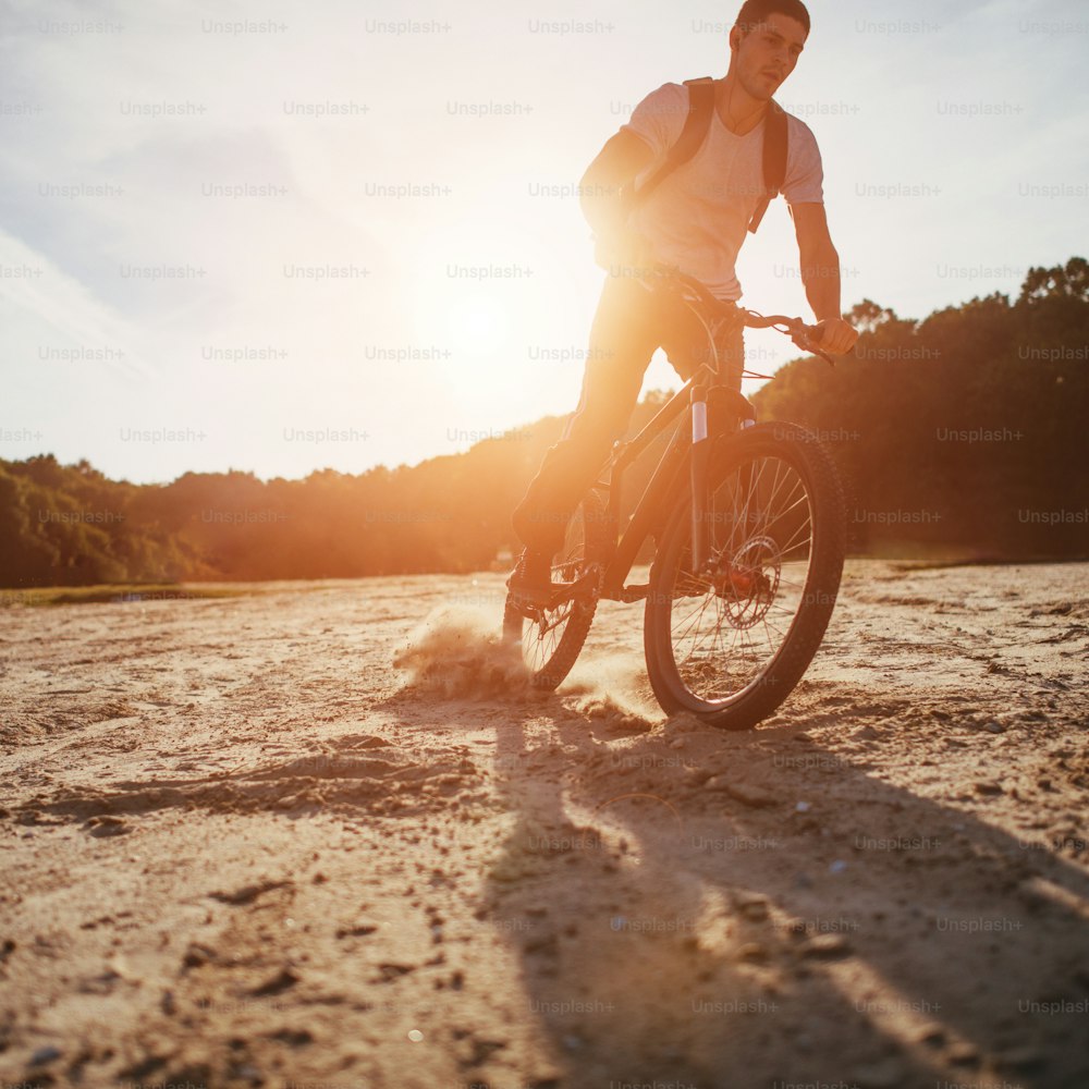 Motociclista atraente andando ao longo da praia ao pôr do sol
