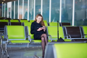 Giovane donna all'aeroporto internazionale, controllando il suo telefono mentre aspetta il suo volo