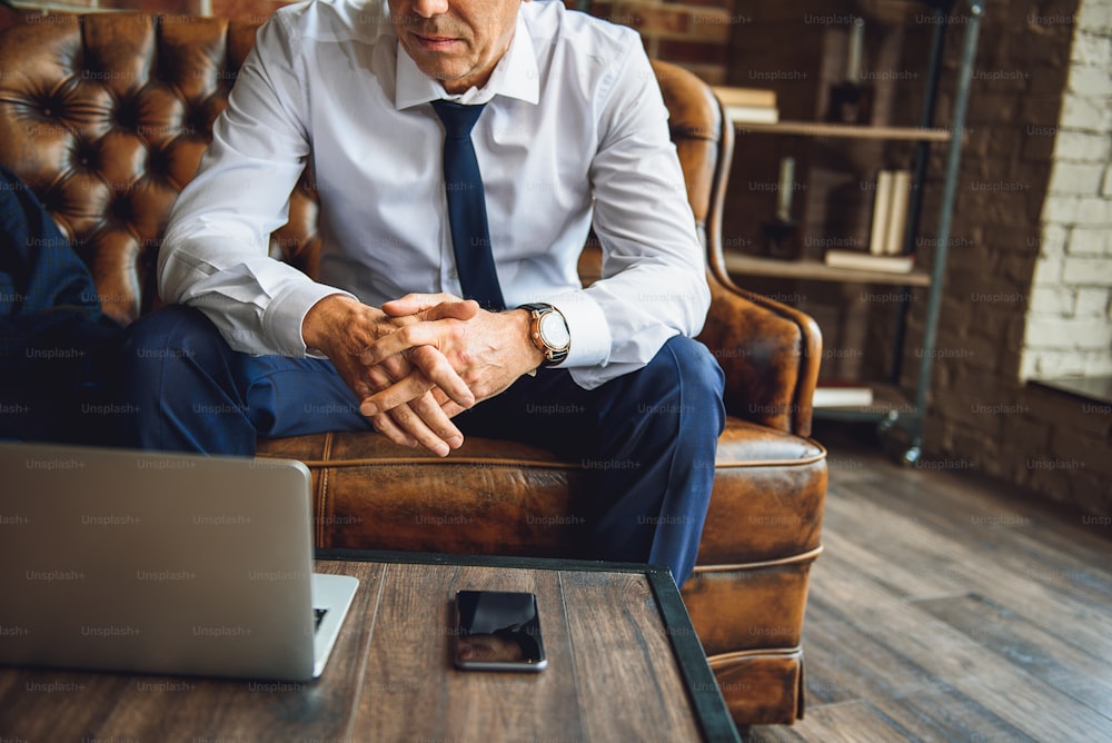 Phone and computer are at table in front of serious male person. He sits near desk