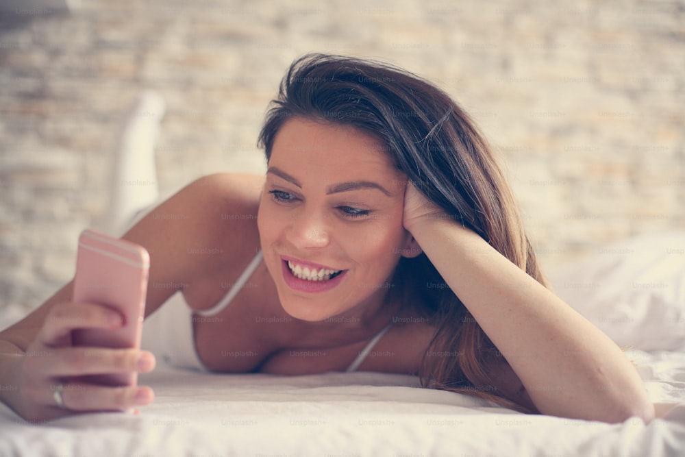 Brunette woman using smart phone in bed.