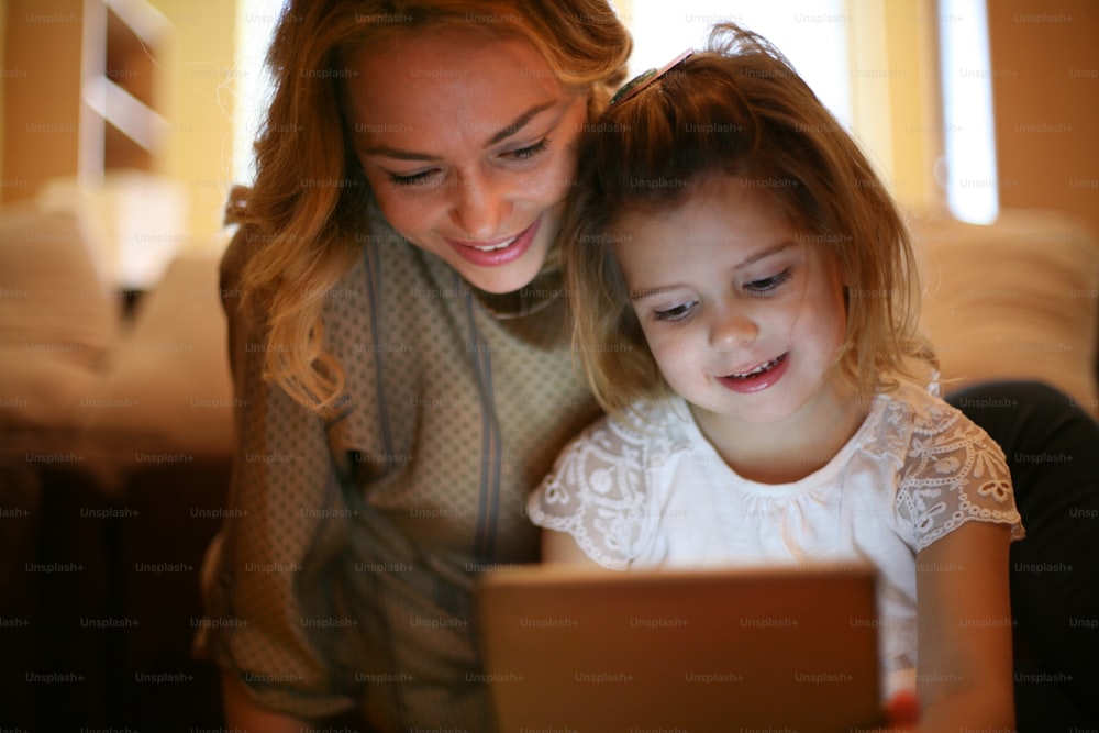 Beautiful girl sitting with her mother on floor and looking at tablet.
