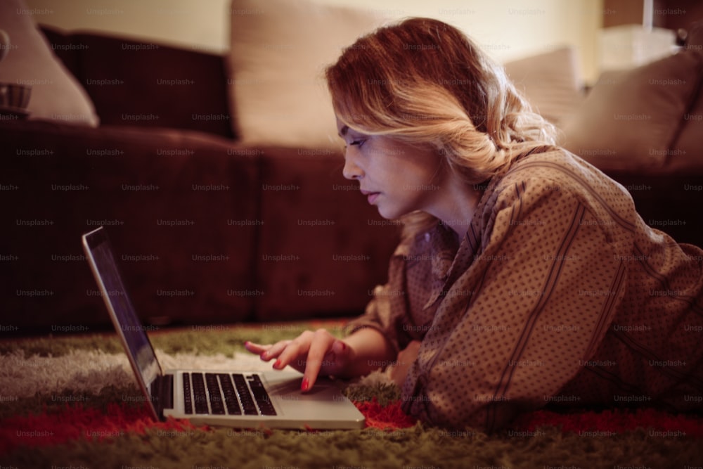 Mulher loira bonita usando seu laptop no conforto de sua sala de estar.