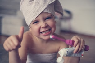 Bambina carina si lava i denti in bagno. Guardando la fotocamera e mostrando ok.