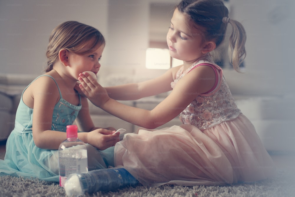 Little girl cleaning face of her small sister at home.