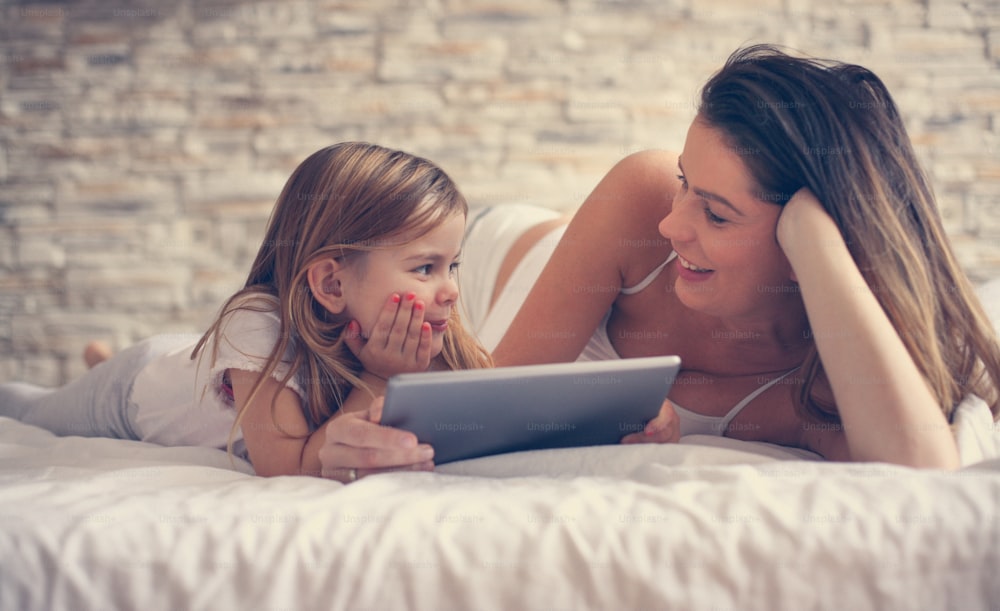 Mujer joven feliz con hija usando una tableta digital en la cama en casa.