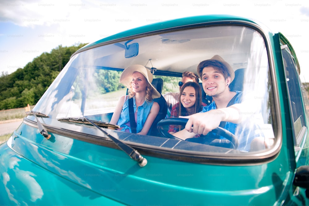 Chico hipster conduciendo una vieja autocaravana con amigos adolescentes, viaje por carretera, día soleado de verano