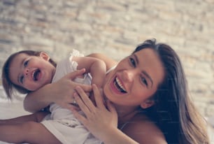 Young mother playing with her baby girl playing in bed.