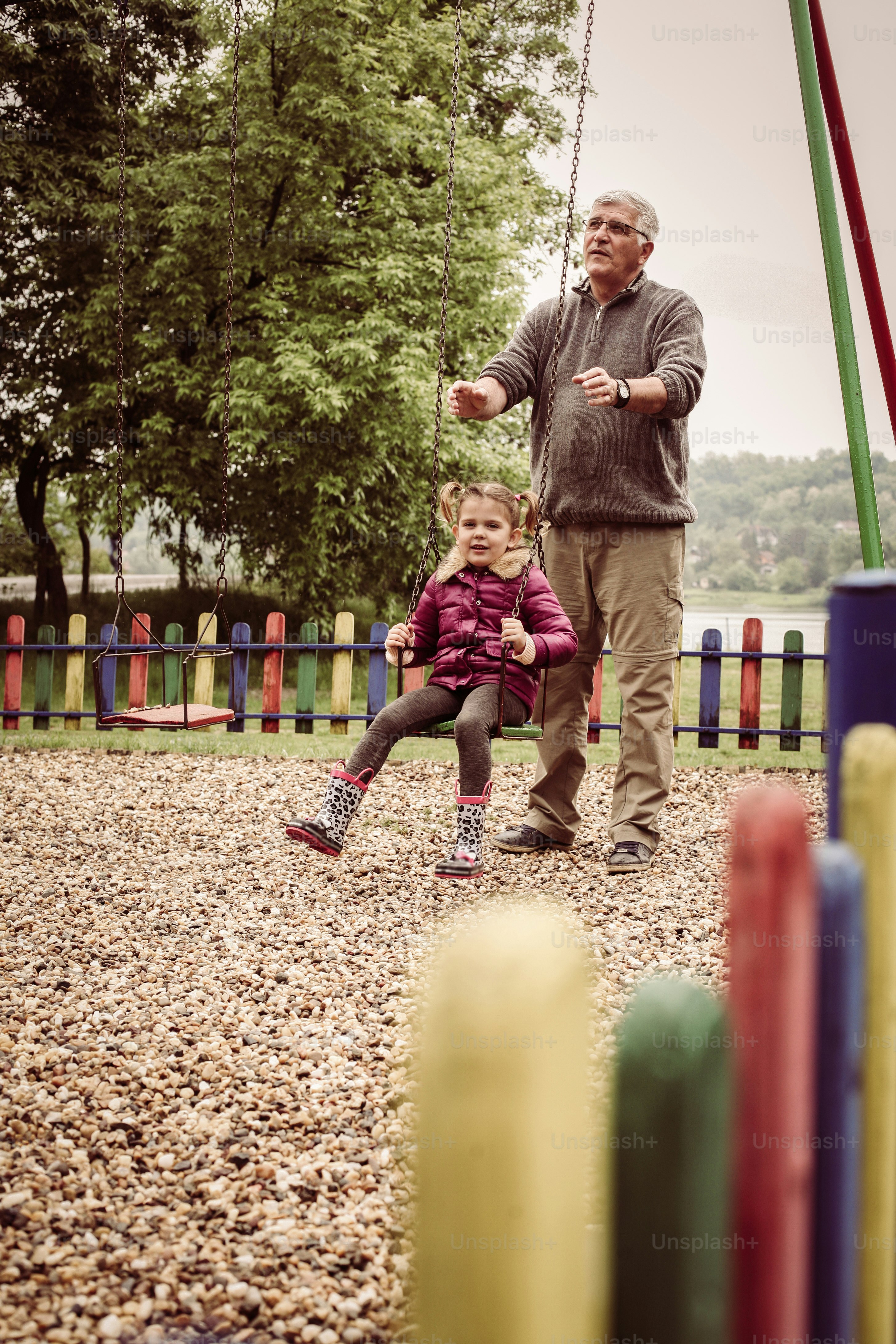 Caucasian grandfather pushing granddaughter on playground swing.