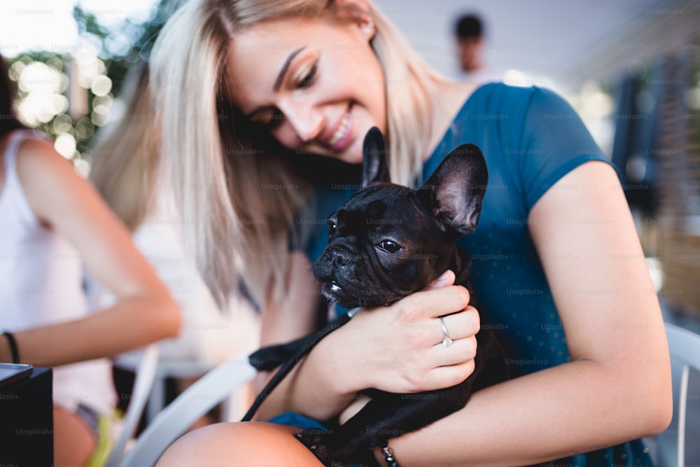 Bella giovane donna seduta in un caffè con il suo adorabile cucciolo di bulldog francese. Città primaverile o estiva all'aperto. Tema persone con cani.