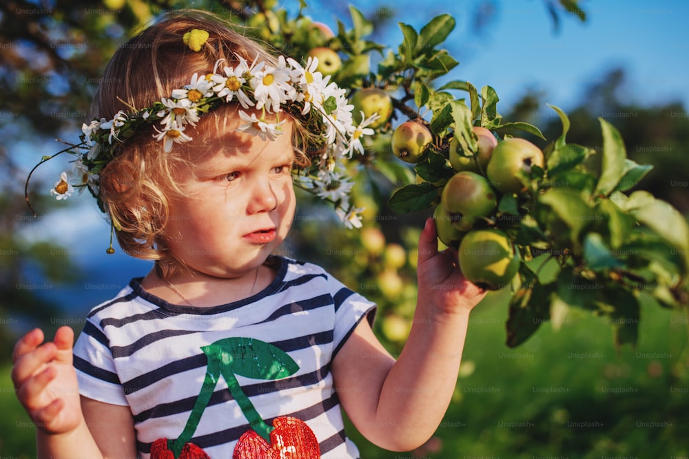 Little cute girl with a wreath on his head in the garden near the tree