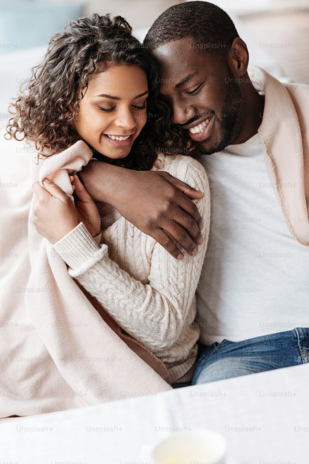 Heureux d’être amoureux. Un jeune couple afro-américain ravi et positif assis dans le café et recouvert d’une couverture tout en exprimant son amour et en se serrant dans ses bras