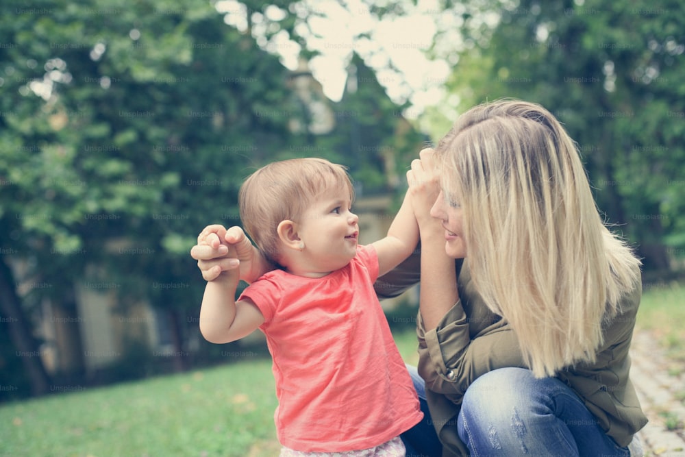 Young mother teaching her daughter to her first steps. Little baby girl.