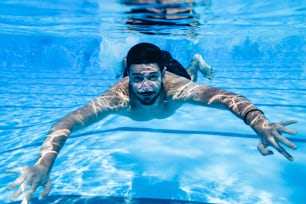 Underwater fun. Two young handsome men swimming underwater and diving in the swimming poll. Sport and leisure.