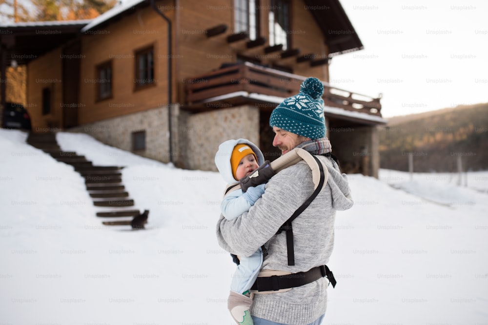 Handsome young father with his son outside on a walk, holding him in baby carrier. Sunny winter nature.
