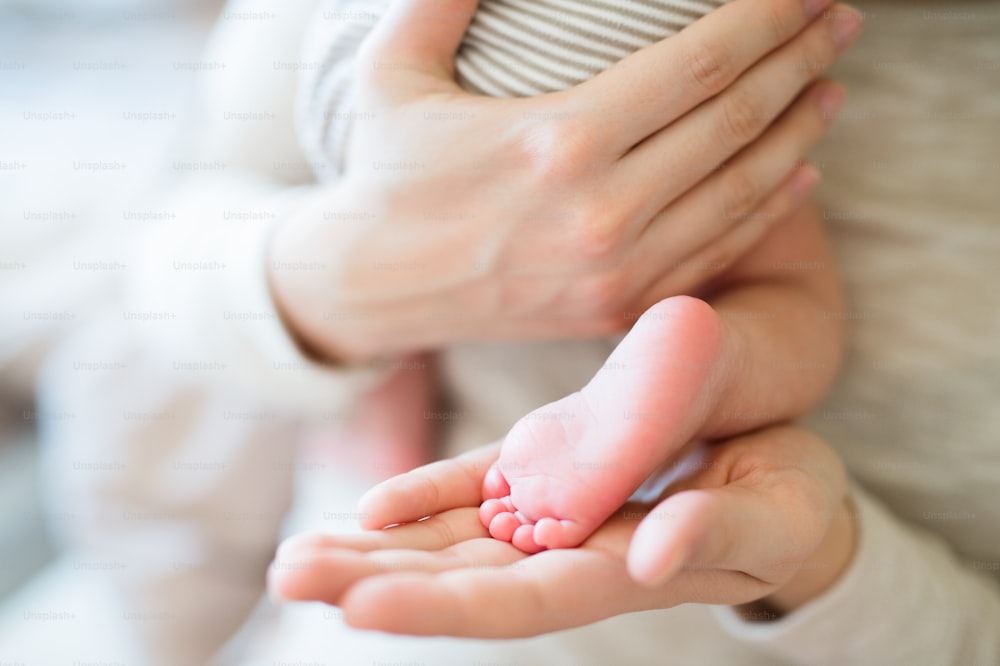 生まれたばかりの赤ん坊の息子を腕に抱き、脚と手をクローズアップした見分けのつかない母親。