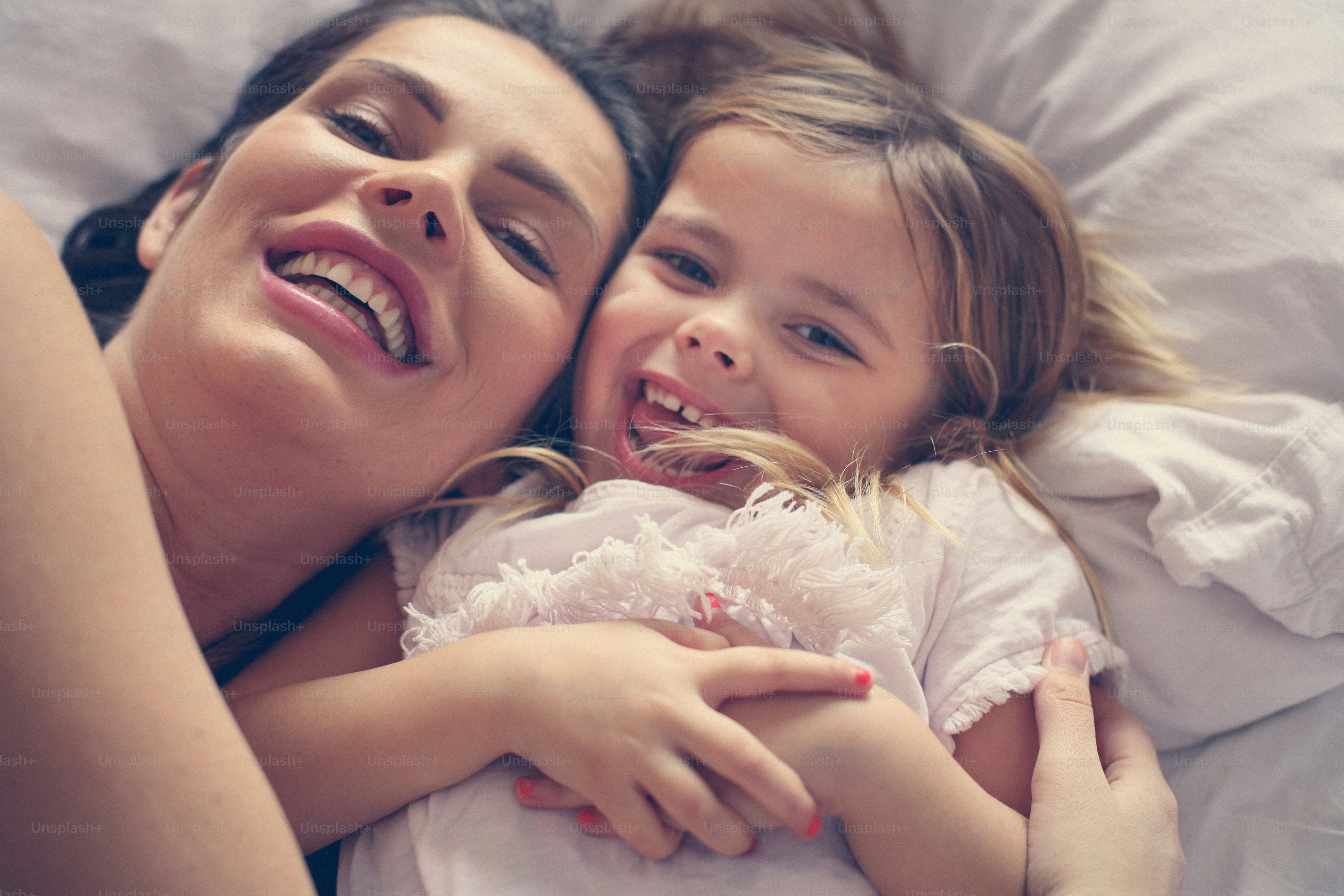 Madre e hija disfrutan en la cama en casa y mirando a la cámara. foto ...