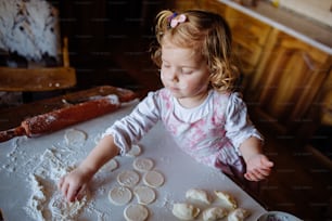 baker girl in knead the dough and shapes cakes in the kitchen