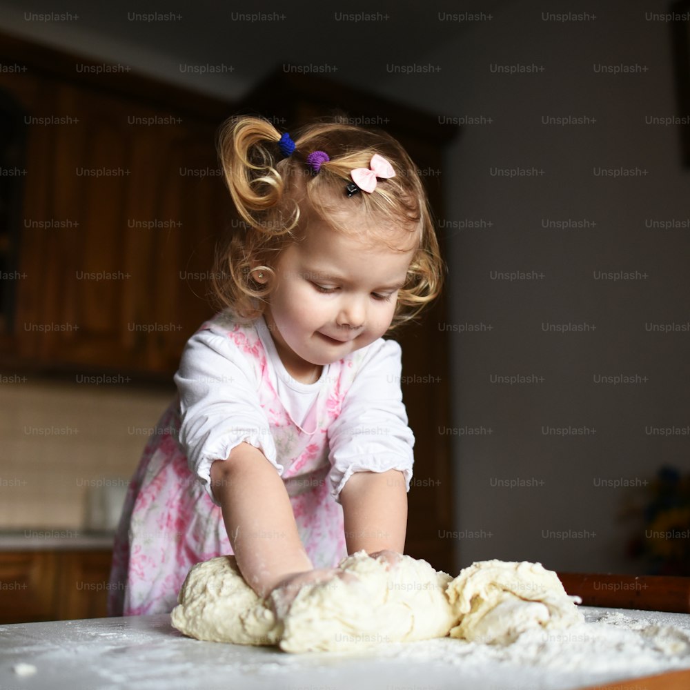 baker girl in knead the dough and shapes cakes in the kitchen