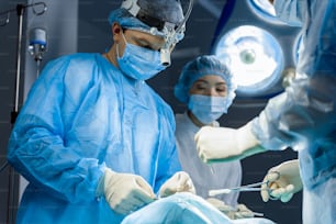 El equipo quirúrgico ocupado está realizando operaciones con la ayuda de equipos médicos. Están de pie alrededor del paciente. Ángulo bajo