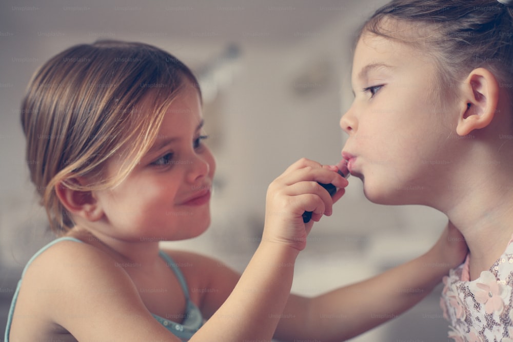 Little girl putting lipstick  to her sister.