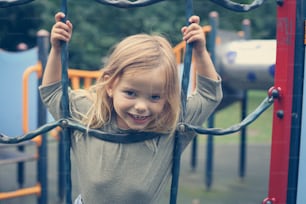 Little girl is climbing at the playground and looking at camera.