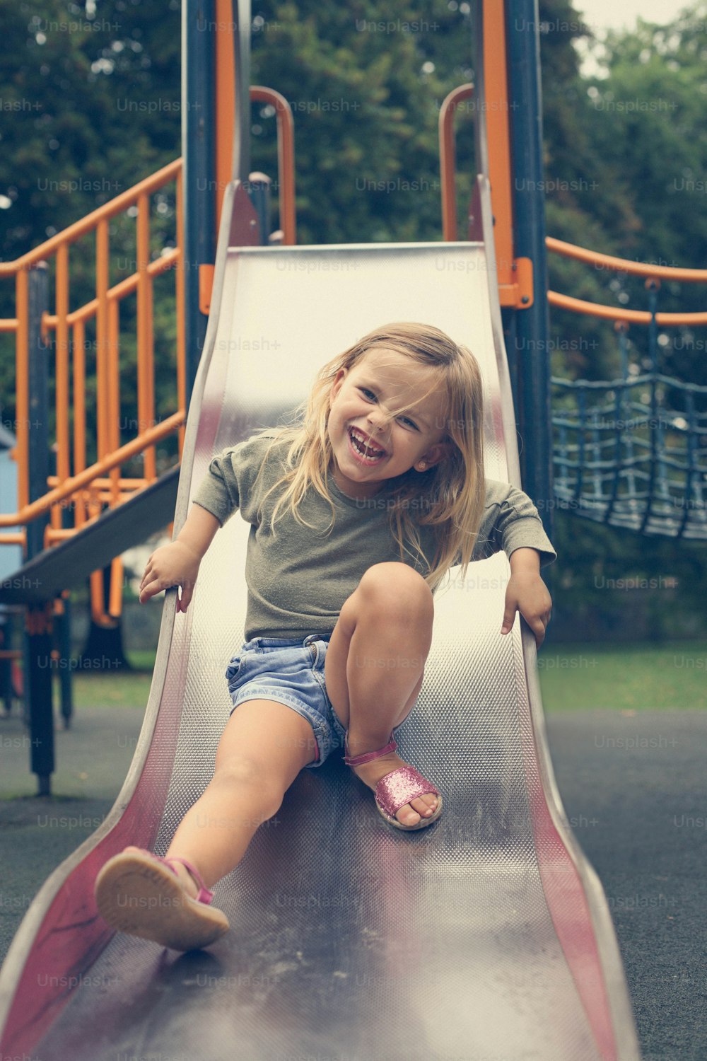 Little girl sliding down a slide in a playground.
