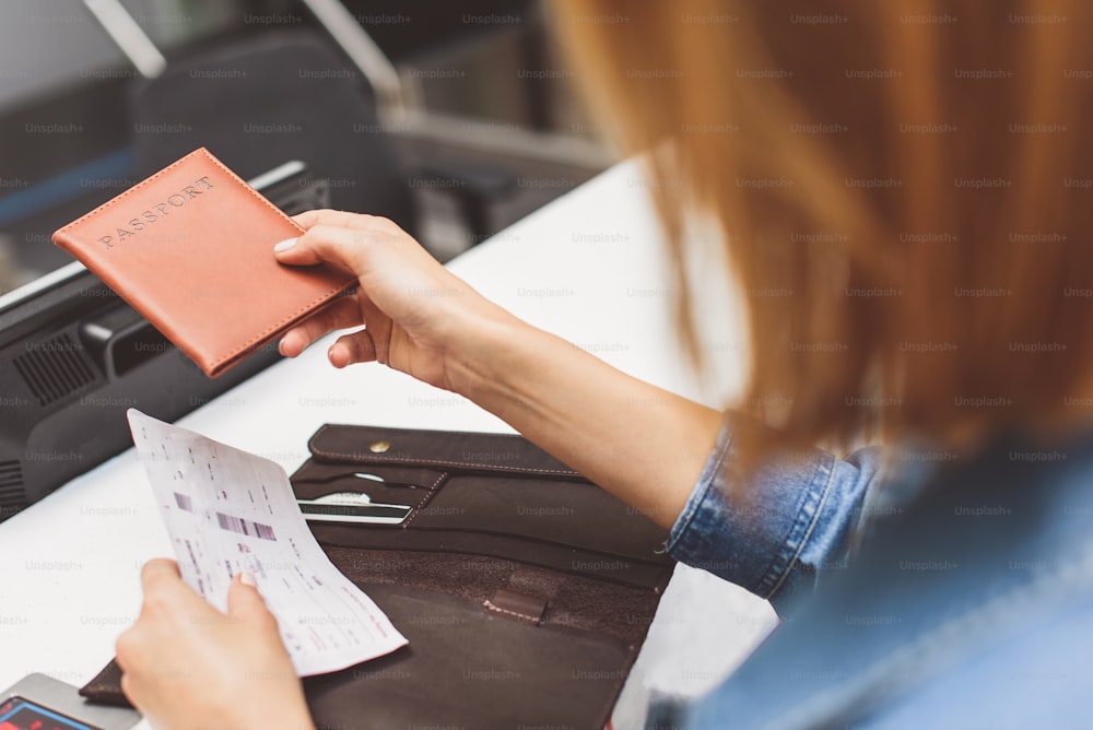 Una giovane passeggera sta consegnando il suo passaporto all'addetto al check-in. Primo piano delle sue mani che tengono il biglietto aereo