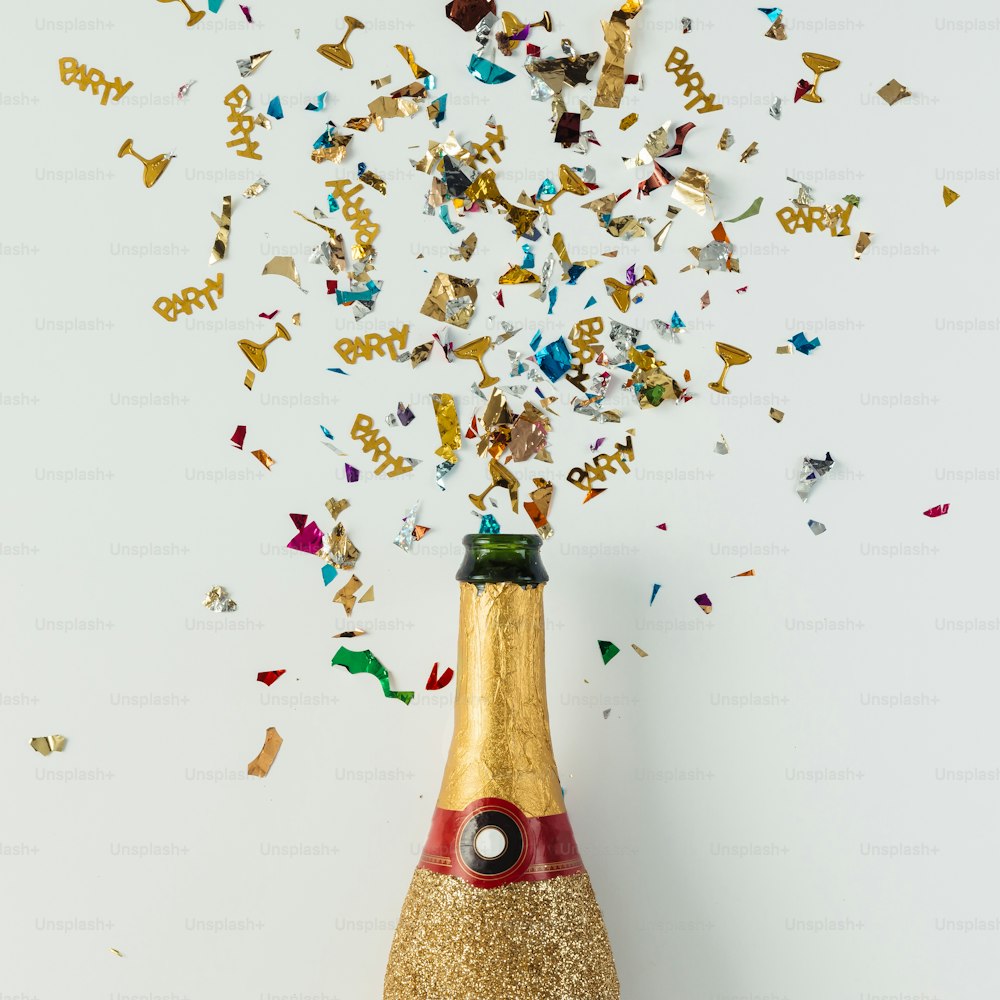 Golden champagne party bottle with confetti on bright background. Flat lay. Celebrate concept.
