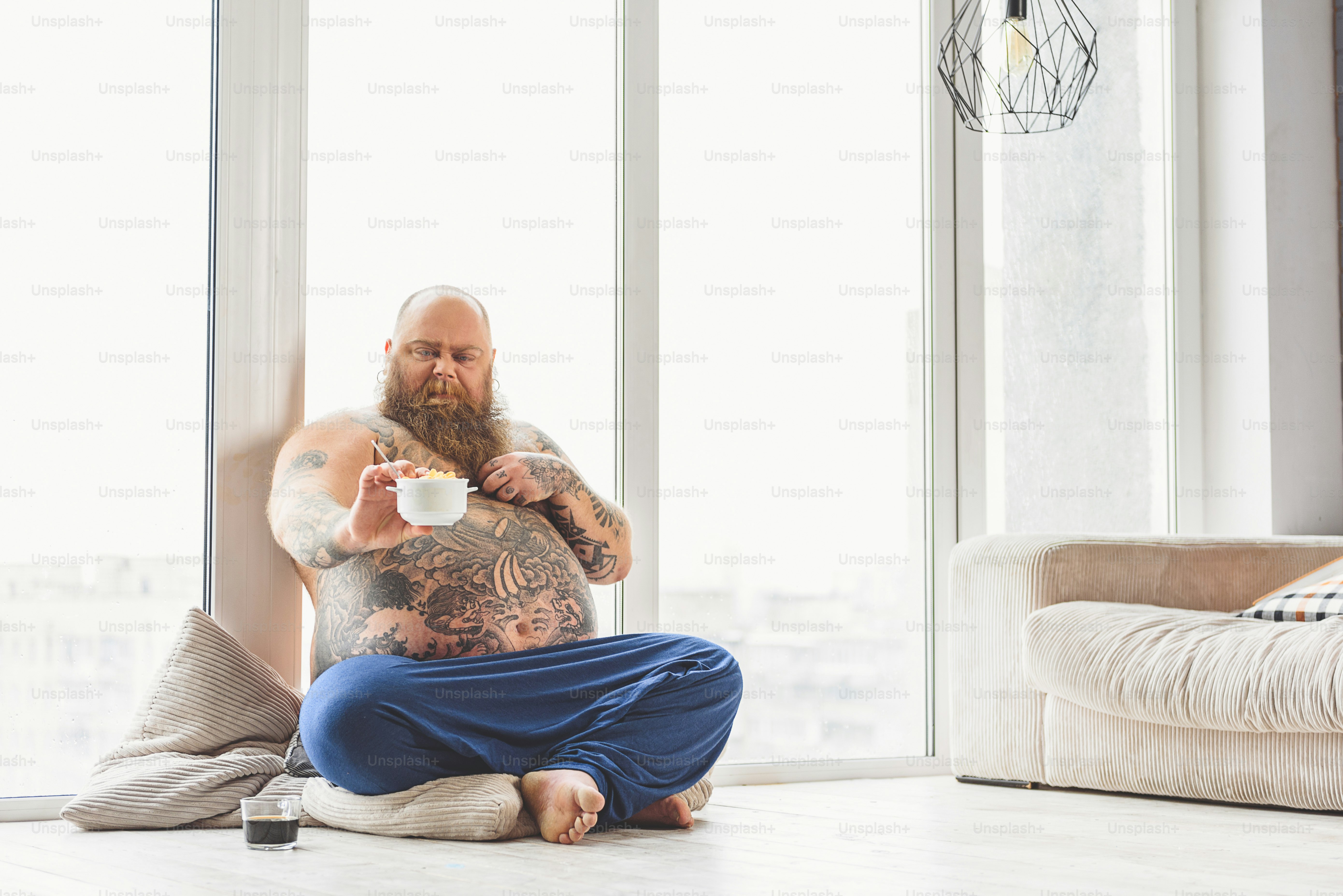I hate healthy food. Mature thick guy is holding bowl of cornflakes and looking at it with disgust. He is sitting near window at home