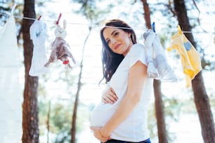 woman hanging baby clothes in linen rope outdoors.